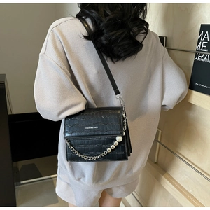 Close-up of black crocodile pattern leather bag with elegant pearl and chain decoration