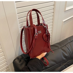 Détail du sac à main bordeaux en cuir ciré avec logo argenté et pendentif en forme de cœur