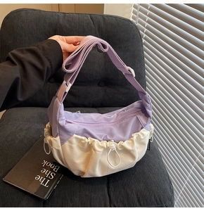Detail view of purple and beige contrast crossbody bag with drawstring on a corduroy chair
