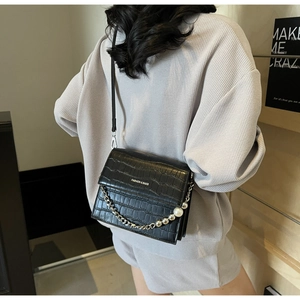 Detail of black faux crocodile skin bag with silver chain and pearl decoration on a model
