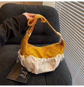 Detail view of yellow and white crossbody dumpling bag on a sofa with wide strap