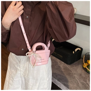 Pink mini crossbody bag featuring a pearl bow charm and glossy leather texture details