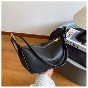 Detail of black pebbled leather half-moon bag with gold zipper and adjustable strap