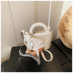 Detail of white mini bucket bag featuring a decorative pearl lace bow and slim strap