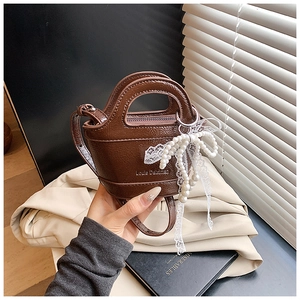 Detail of a brown mini crossbody bag with a pearl lace bow and smooth faux leather finish