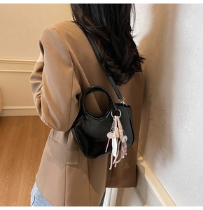 Detalle de bolso tote de charol negro brillante con colgantes y correa de bandolera
