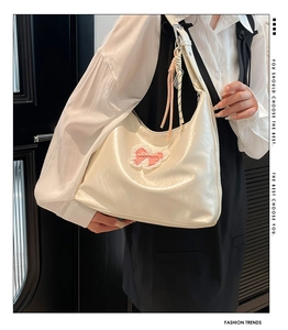 Detail of cream leather tote bag featuring pink lace bow and woven shoulder strap