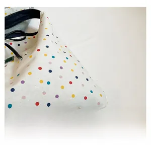 Close-up of white fabric tote with colorful polka dots and durable black strap texture