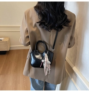 Vista trasera detallada de un bolso de charol negro brillante con un colgante de borla rosa