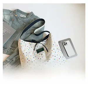 Detail view of canvas tote bag featuring colorful polka dots and a black bow accent