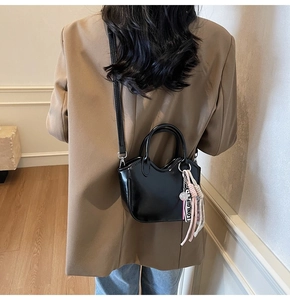 Detalle del bolso de charol negro brillante con bordes ondulados y colgante de cinta