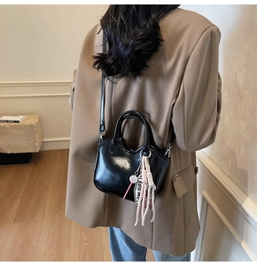 Detalle del bolso negro brillante con etiqueta de letras y adorno trenzado de diseño