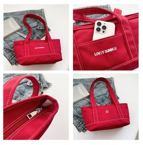 Detail view of red canvas tote bag showing zipper closure, outer pocket, and embroidery