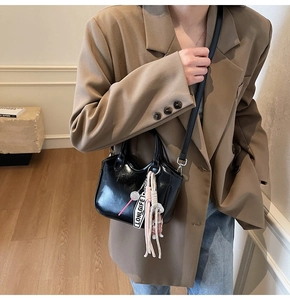 Bolso tote de charol negro a la moda combinado con traje y colgante tejido decorativo