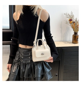 Primo piano di una borsa a tracolla color crema con chiusura rotante in metallo su modella