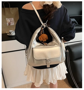 Silver large-capacity tote backpack with plush bear charm worn by a seated model