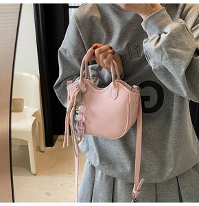 Detalle de bolso de cuero rosa claro con borla y bandolera sostenido por una modelo