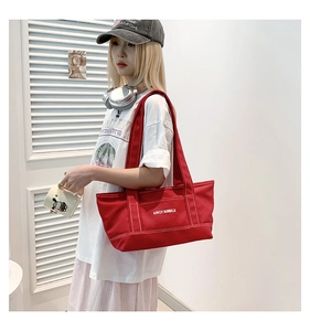 Detail of red canvas tote bag with Lovey Summer embroidery worn by a model