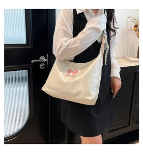 Detail of off-white hobo bag with pink lace bow patch and woven strap accessory