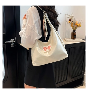 Detail of cream white tote bag with pink bow and tassel pendant in lifestyle setting