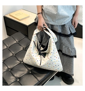 Detail of colorful polka dot pattern and black lace-up tie on a white hobo tote bag