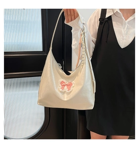 Close-up of white leather hobo bag with pink bow lace charm and woven strap detail
