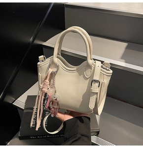 Detalle de bolso tipo cubo color crema con colgante de perro y hebilla metálica