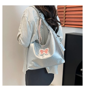 Detail of silver metallic hobo bag with pink lace bow applique and woven charm