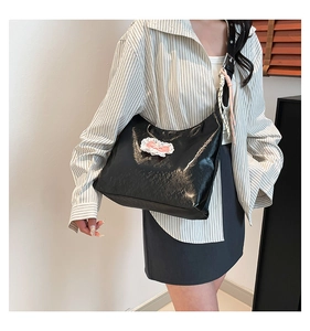 Detail of glossy black patent leather tote bag with a pink and white lace bow accessory
