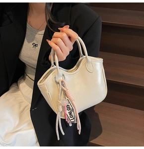 Detalle de un bolso de piel crema con borde ondulado y un colgante de nudo