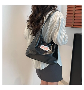 Detail of a large black glossy tote bag with a pink lace bow on a model's shoulder