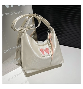 Detail of a creamy white glossy tote bag with a pink lace bow and woven rope pendant