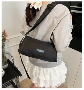 Détail d'un sac oreiller en nylon noir avec écusson logo et large bandoulière lettrée