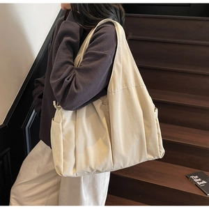 Close-up of beige canvas tote bag with pleated details and wide shoulder strap