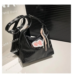 Detail of black patent leather tote bag with pink lace-edged bow and adjustable strap