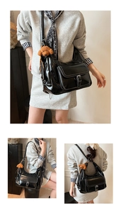 Detail view of black crescent tote bag featuring white contrast stitching and plush bear charm