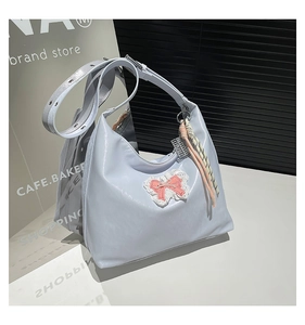 Detail of light blue patent leather tote bag featuring a white lace bow patch and metal buckle