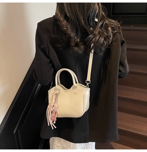 Vista de detalle del bolso crema con bordes ondulados y colgante de oso llevado por modelo