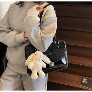 Detailed view of a black patent leather messenger bag with a white plush rabbit keychain