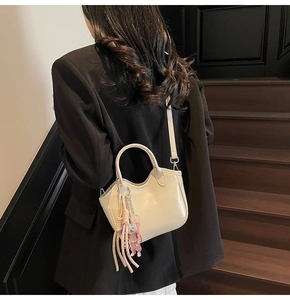 Detalle de mini bolso bombonera de cuero crema con borla y borde superior ondulado