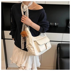 Macro detail of ivory PU leather tote bag featuring a front flap pocket and a plush bear charm