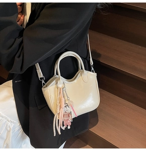 Detalle del bolso tipo cubo crema con colgante de perrito y borla tejida en un modelo