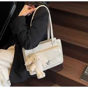 Detailed view of white patent leather shoulder bag with metallic lock and plush bunny pendant