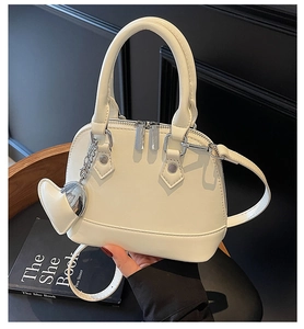 Close-up of white leather shell bag with silver hardware and heart-shaped pendant detail