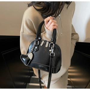 Detail of glossy black shell bag featuring silver hardware and heart charm attachment
