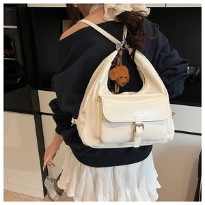 White minimalist hobo bag with a plush puppy charm and silver buckle detail on a model