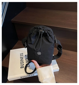 Detail of black nylon drawstring crossbody bag resting on a book with hand for scale