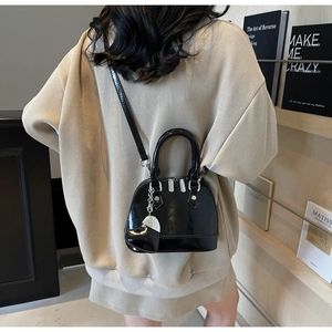 Glossy black shell bag with heart charm shown from a back view on a female model
