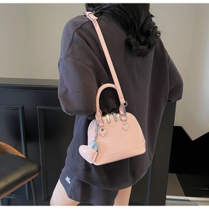 Pink patent leather shell bag with heart charm shown on model for size perspective