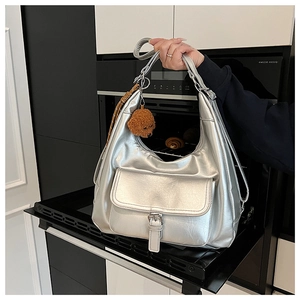 Detail of silver metallic hobo bag with buckled pocket and plush bear charm decoration